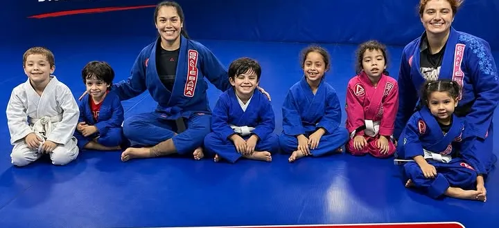 Niños sentados en el tatami junto a dos profesoras en una clase de BJJ Kids